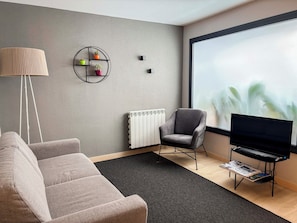 Una sala moderna con un sofá gris, un sillón gris, una lámpara de pie, un televisor sobre un mueble bajo y un radiador.