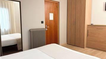 Habitación de hotel con cama, armario, radiador y puerta con un cartel.