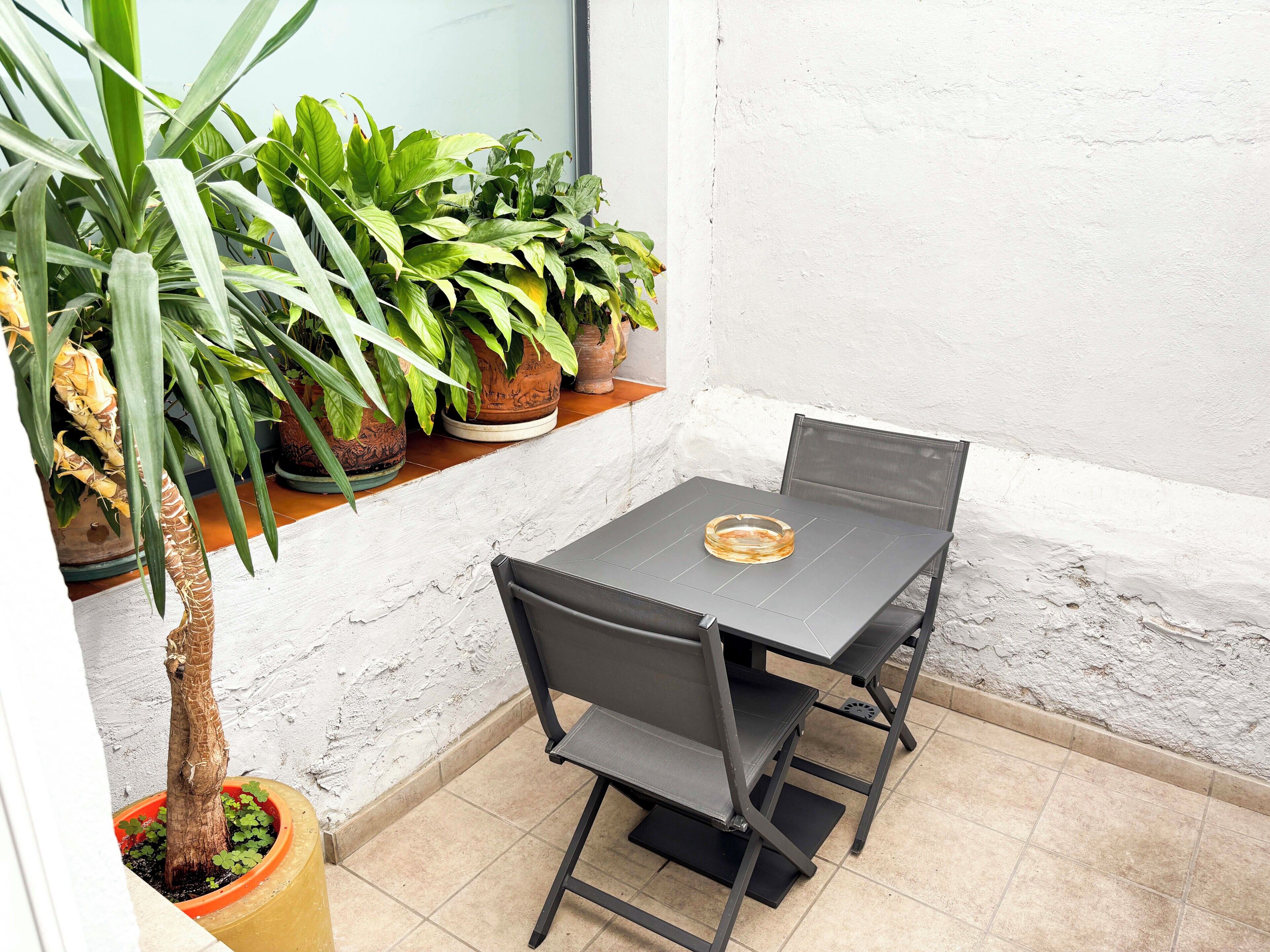 A small outdoor patio with a table and chairs, surrounded by potted plants.