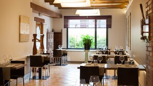 Un restaurante con vigas de madera a la vista, amplios ventanales con vistas y mesas con sillas ordenadas.