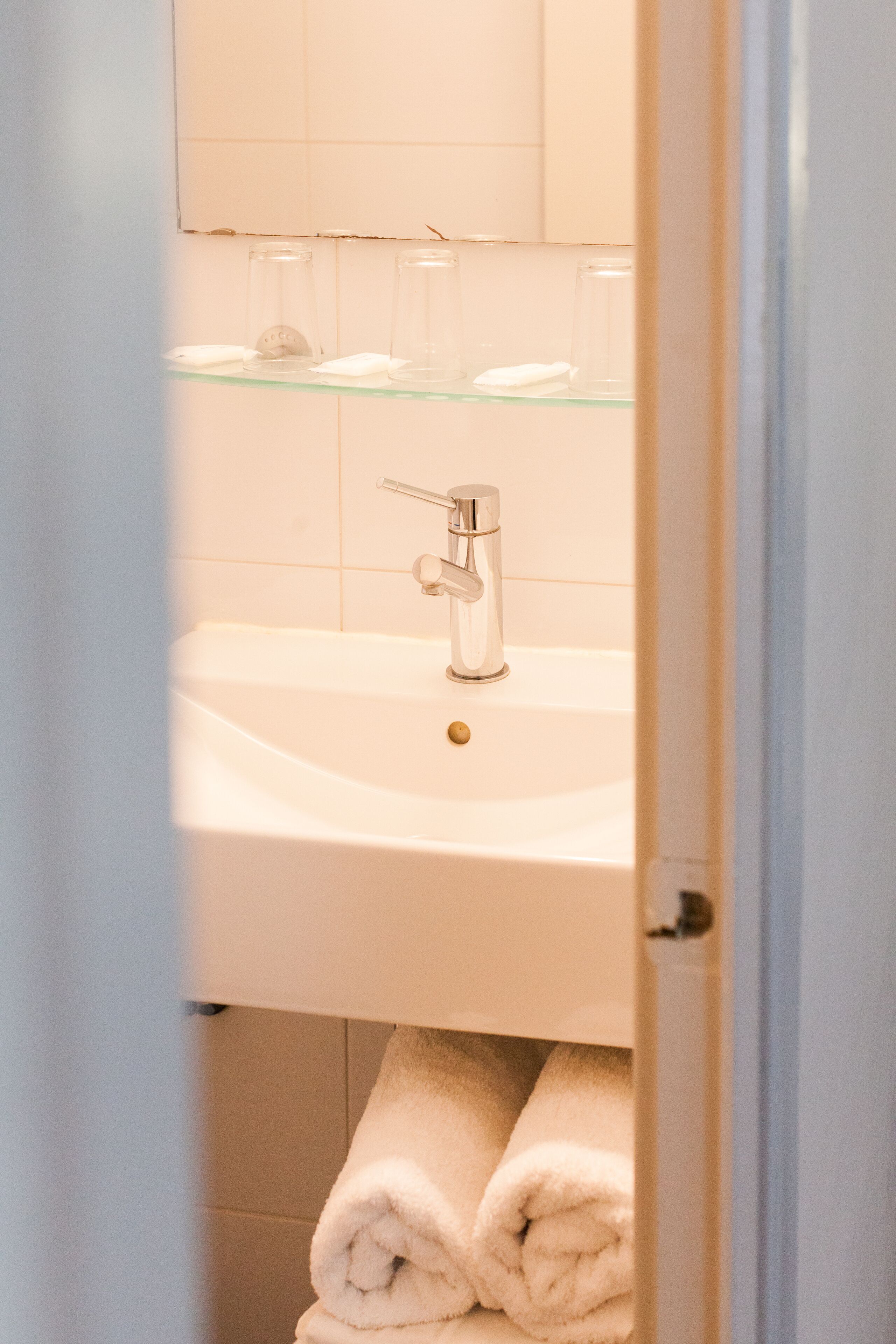 A bathroom with a sink, mirror, and glass shelves.