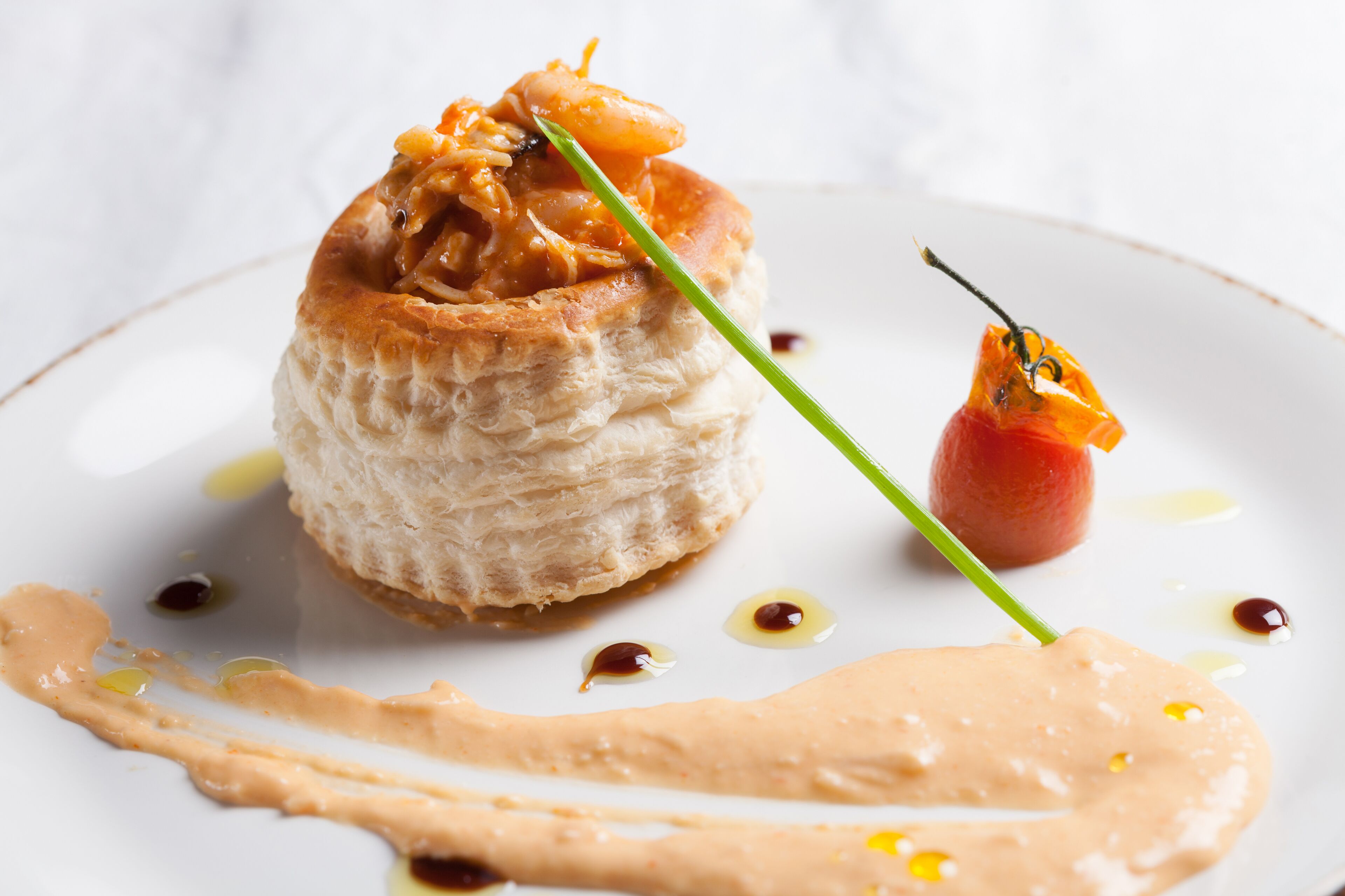 Un postre con base de hojaldre, salsa y una pequeña decoración de tomate en un plato.