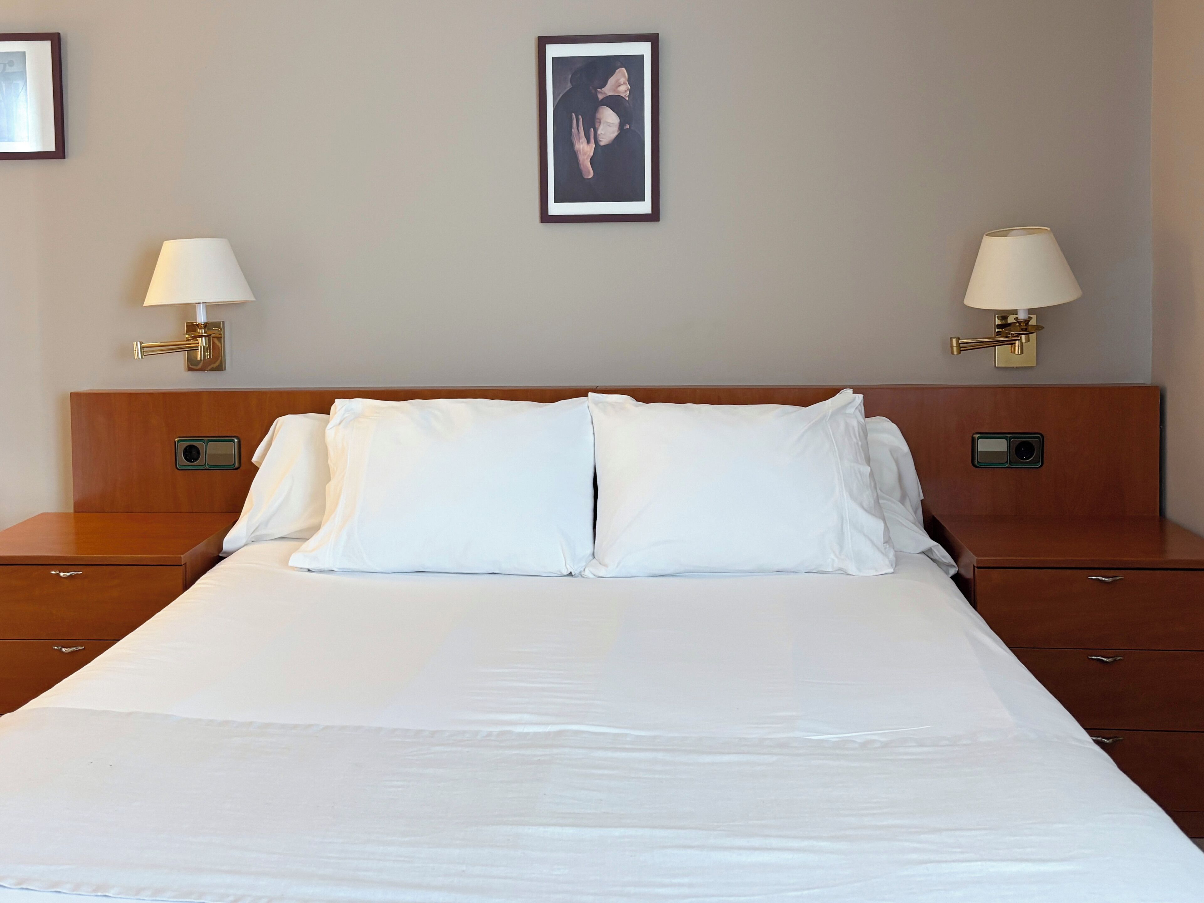 A hotel room with a large bed, two bedside tables, and two wall-mounted lamps.