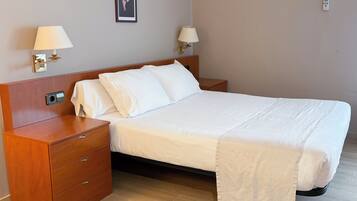 A neatly made bed with white linens, a wooden nightstand with a lamp, and a wall-mounted picture.