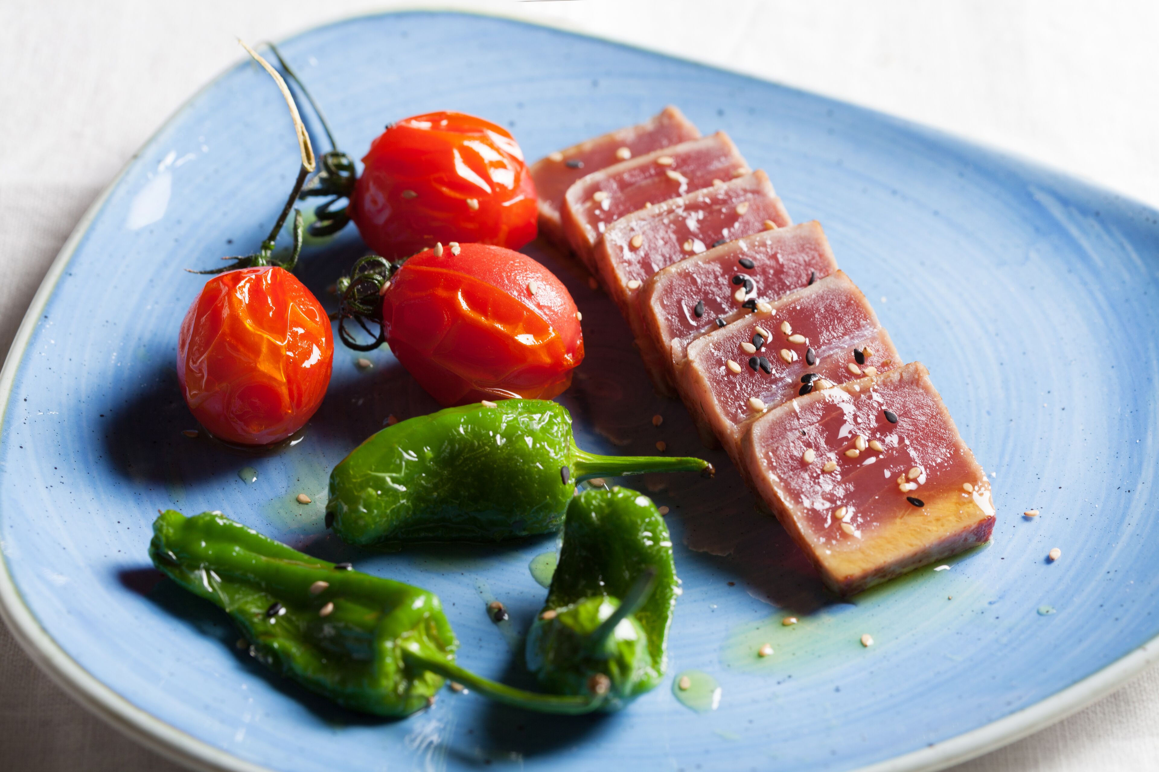 A plate with sashimi, cherry tomatoes, and green chili peppers.