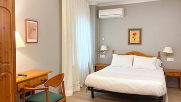 Habitación de hotel con cama, mesitas de noche, escritorio, silla, aire acondicionado y dos lámparas de pared.