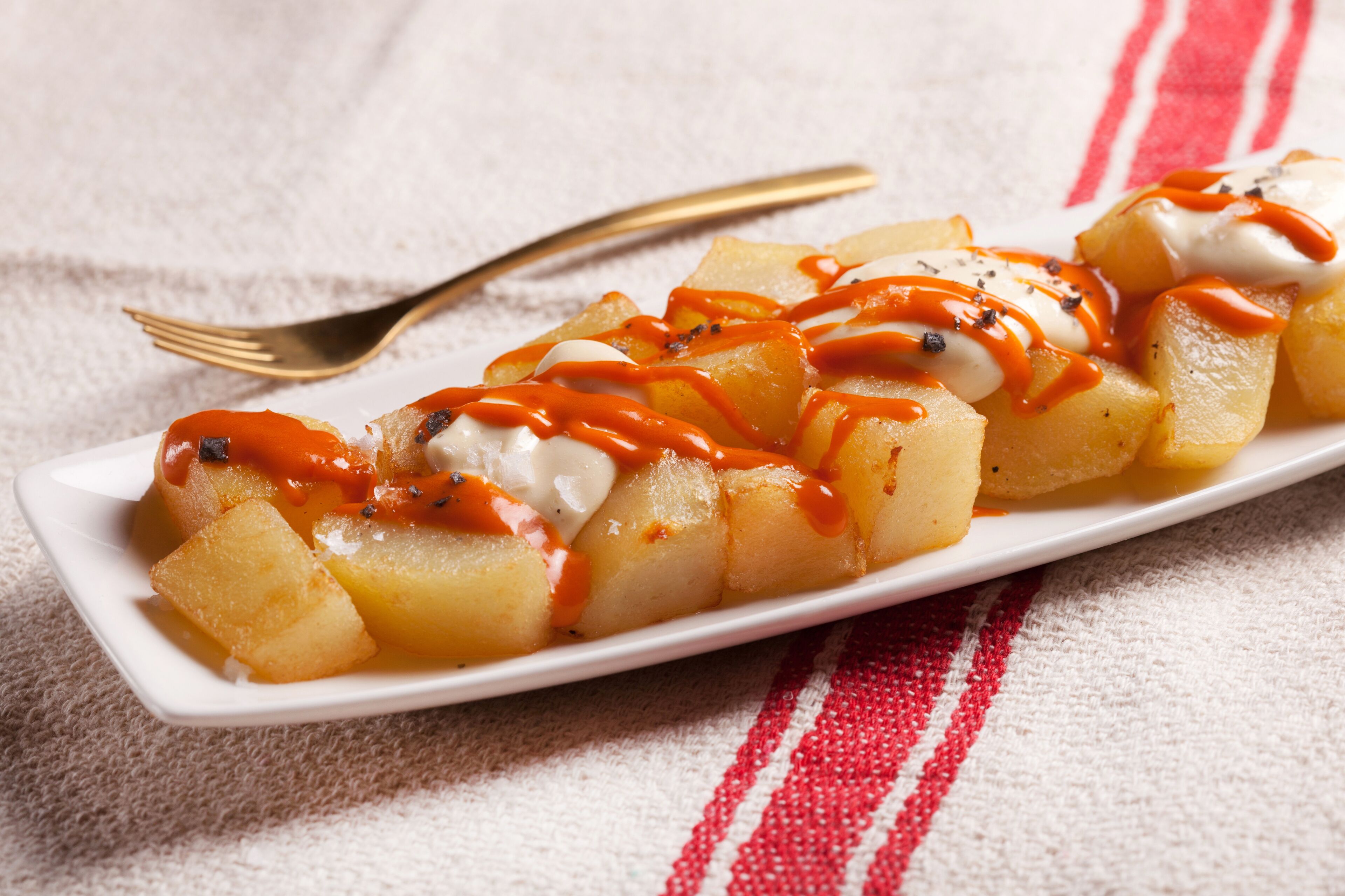 A white rectangular plate with cubed food items, drizzled with sauce and sprinkled with black seeds, on a white cloth with red stripes.