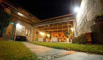 Un patio al aire libre con un muro de piedra, una zona cubierta para sentarse y un camino que lleva a la entrada.