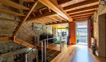 Un interior rústico con chimenea de piedra, escalera de madera y una zona de estar acogedora.