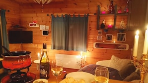L’intérieur chaleureux d’un chalet en bois, avec une table à manger dressée pour deux personnes, créant une ambiance intime grâce à la lumière des bougies.