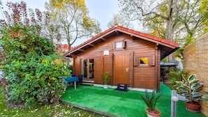 Une cabane en bois avec une pelouse verte, une petite table et des plantes en pot.