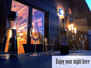A table set with a wine bottle, glasses, and a candle holder outside a building at night. - Dreamy Garden Lodge Center Berlin (Berlin)