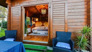Une cabane en bois avec un intérieur chaleureux, un lit, un coin repas et une petite véranda avec des chaises et une table.