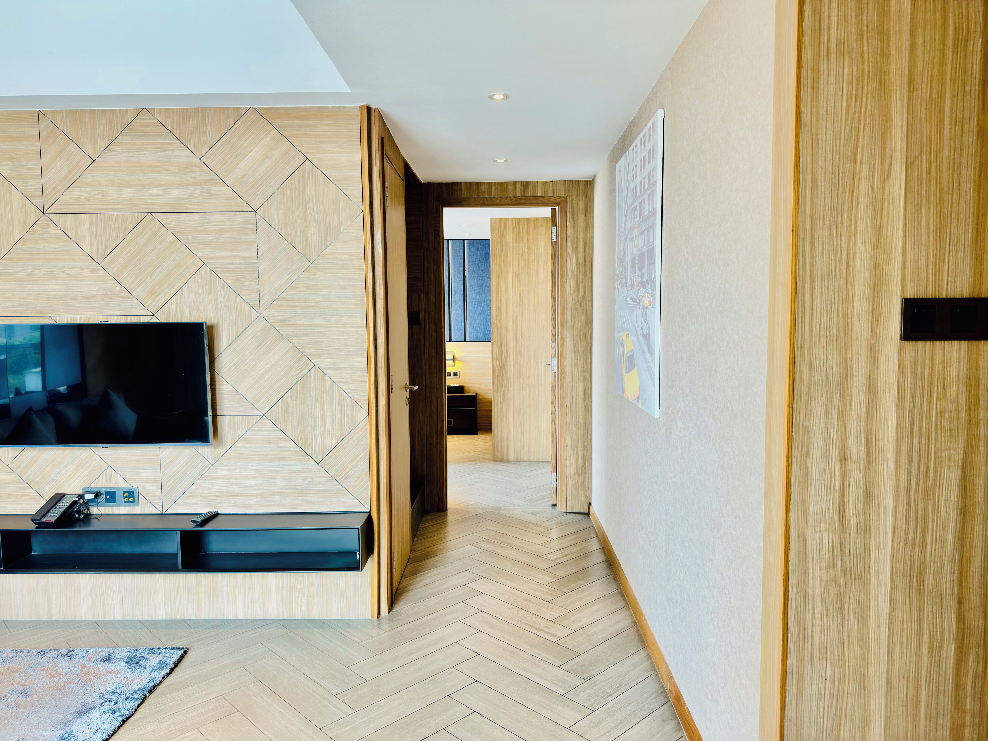 Ein modernes Interieur mit Fischgrätparkett, einem Flachbildfernseher, einer Holzpaneelausstattung und einem Gang zu einem anderen Raum.
