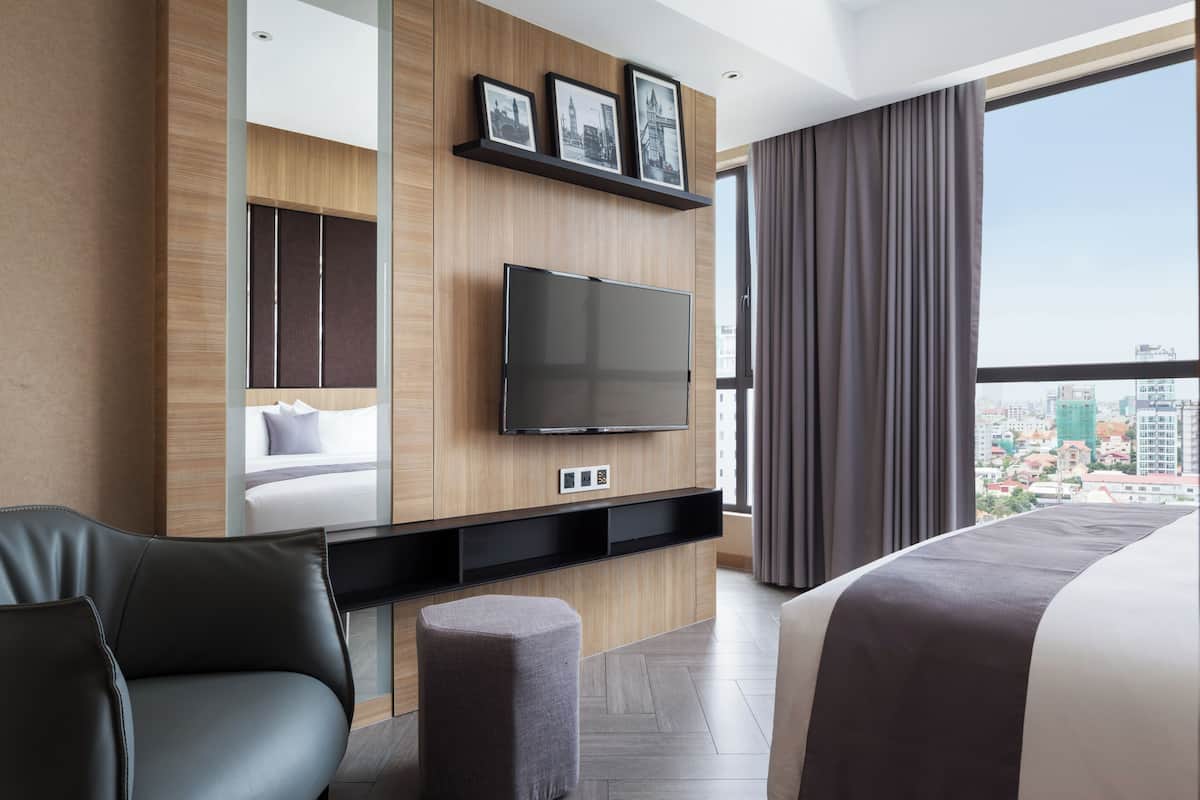Une chambre d’hôtel moderne équipée d’un lit, d’un canapé, d’un téléviseur fixé au mur et offrant une vue sur la ville.