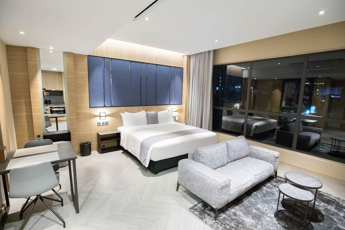 Une chambre d’hôtel moderne, dotée d’un grand lit, d’un canapé, d’un bureau et offrant une vue sur la ville la nuit.