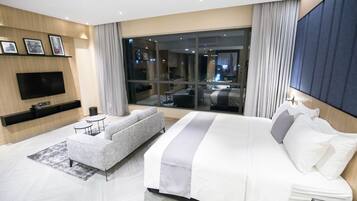 A modern hotel room with a large bed, a sofa, a flat-screen TV, and a large window offering a city view.