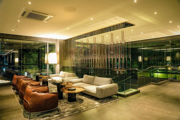 A modern interior with a sofa, leather chairs, and a glass railing overlooking a pool.