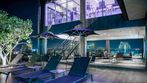 Una terrazza panoramica con lettini, ombrelloni, una scala e vista sulla città.