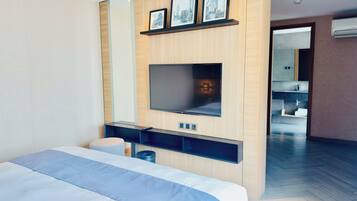 Ett modernt hotellrum med en stor säng, en platt-TV som är monterad på en träpanel, ett litet skrivbord med en stol och ett badrum som syns genom en öppen dörr.