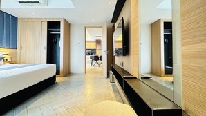 Una camera d'albergo moderna con un letto, una toeletta con specchio, una TV a schermo piatto e un angolo cottura sullo sfondo.