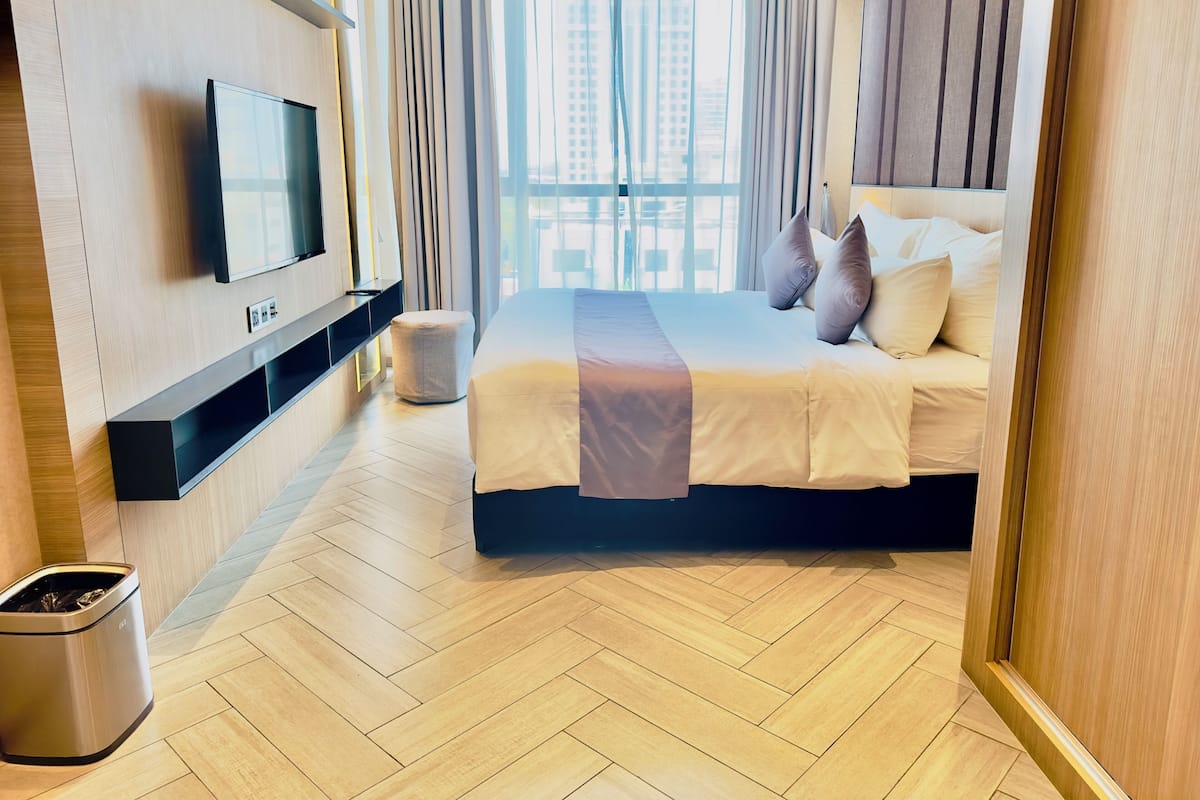 Une chambre d’hôtel moderne avec un grand lit, un téléviseur fixé au mur et une vue sur la ville grâce à de grandes fenêtres.