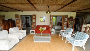 Een ruime woonkamer met een hoge plafond, een rode bank in het midden, witte fauteuils en een salontafel.