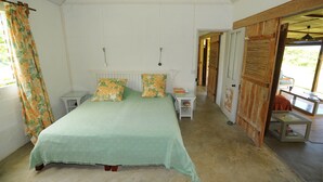 Een slaapkamer met een bed, nachtkastjes, een raam met gordijnen en een deur naar een andere kamer.
