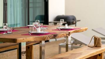 A wooden dining table set with pink placemats and white plates, glasses, and cutlery.