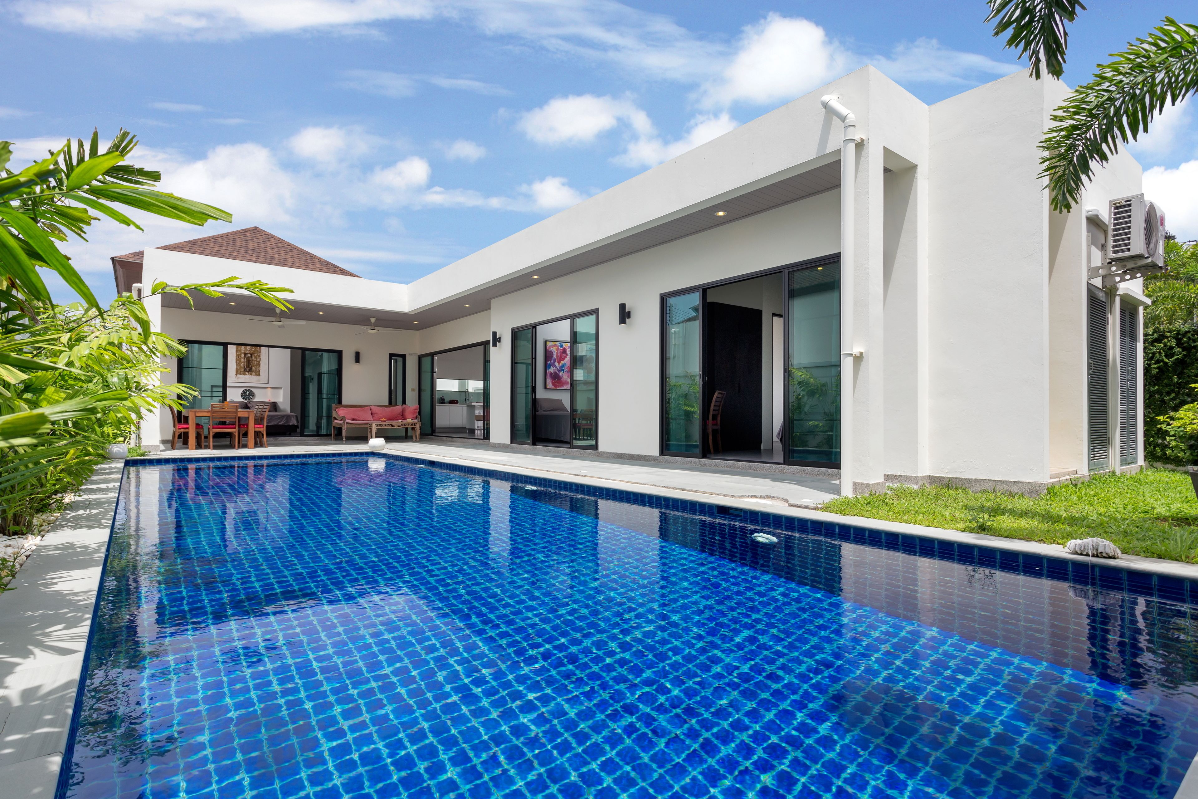 Une maison moderne dotée d’une piscine, de grandes fenêtres et d’un espace patio.