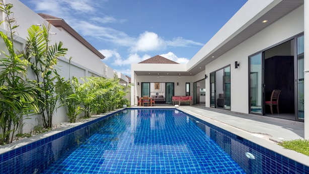 A modern pool area with a clear blue pool, surrounded by white walls and large glass doors. - Large 3BR Villa with Big Pool by Intira (Rawai)