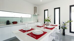A modern kitchen with white cabinetry, a central island with red placemats, and a large window providing natural light. - Large 3BR Villa with Big Pool by Intira (Rawai)