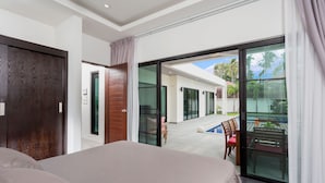 A modern hotel room with a large bed, a sliding glass door leading to a balcony with a pool and outdoor furniture. - Large 3BR Villa with Big Pool by Intira (Rawai)