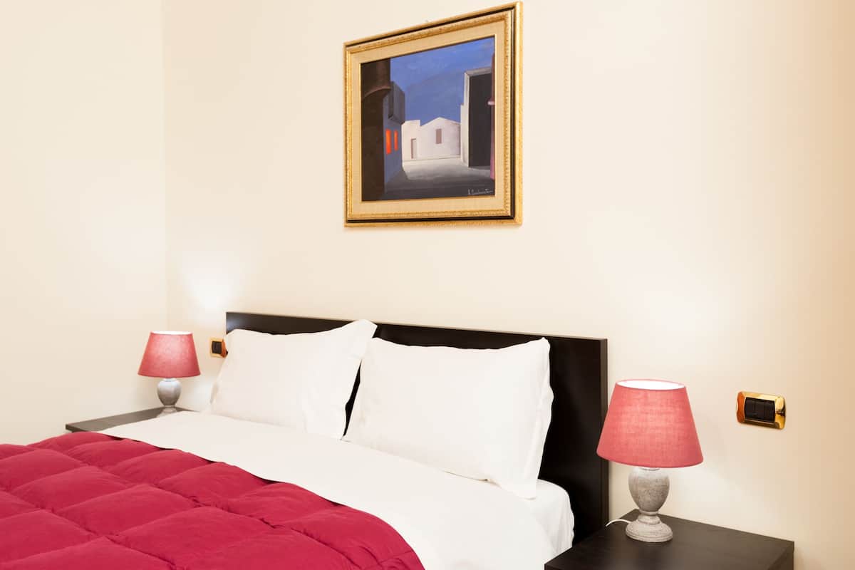 Une chambre d’hôtel avec un lit, deux lampes de chevet, un tableau au mur et un interrupteur près du lit.