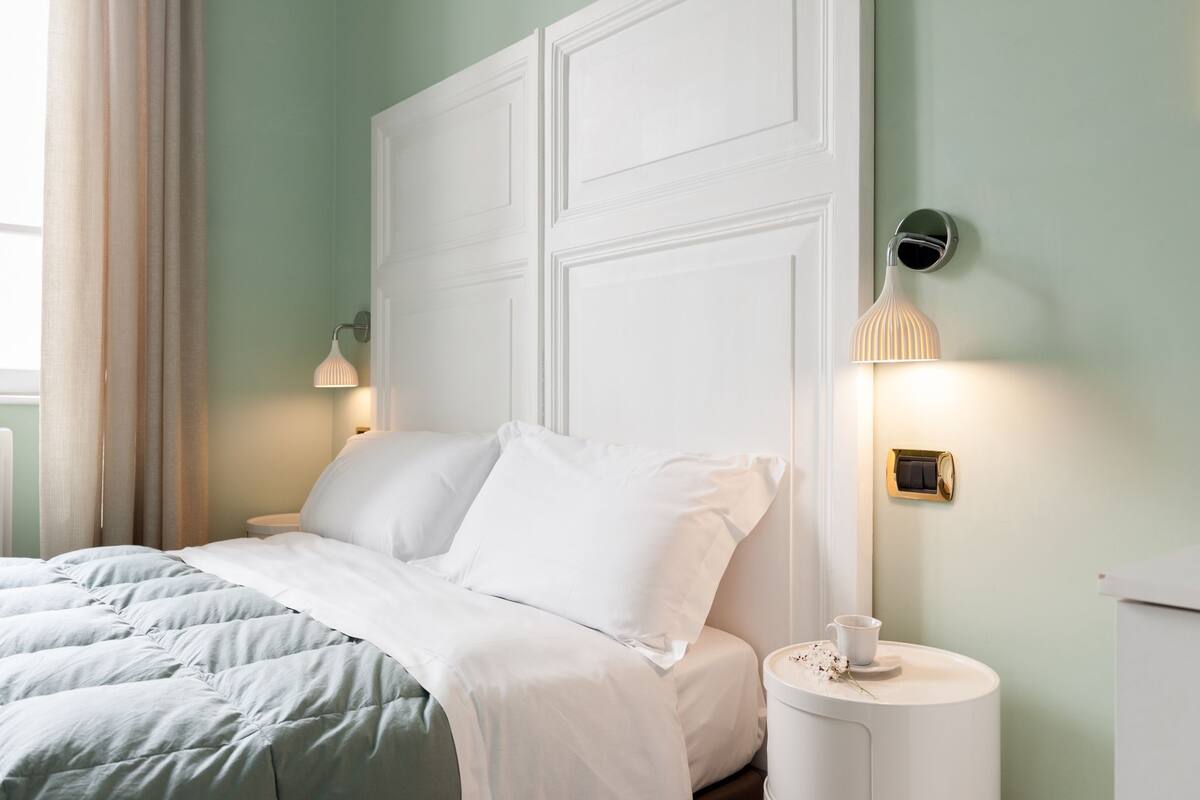 Un lit bien fait, avec une literie blanche, une table de chevet avec une lampe et un luminaire fixé au mur.
