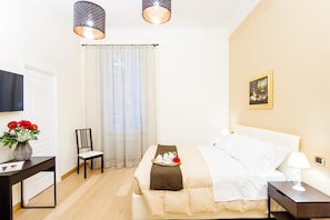 Een hotelkamer met een bed, een stoel, een bureau, een televisie en een schilderij aan de muur.