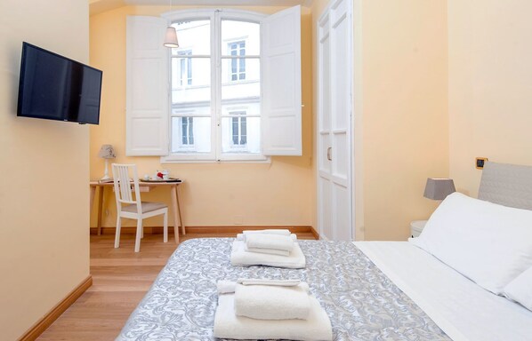 Een hotelkamer met een bed, een bureau, een stoel, een televisie en een raam met witte luiken.