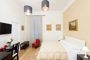 Een hotelkamer met een bed, een bureau met een stoel, een rode stoel, een televisie en twee schilderijen aan de muur.