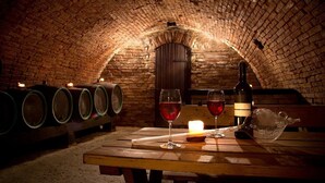 A cellar with wooden barrels, a bottle of wine, glasses, and a candle on a wooden table. - Il Palazzo Boutique B&B (Montalcino)