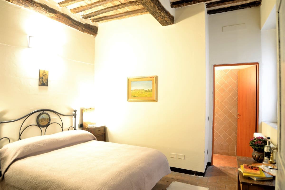 Ein Schlafzimmer mit einem Bett, einem Nachttisch, einem Wandbild und einer Tür zu einem anderen Raum.