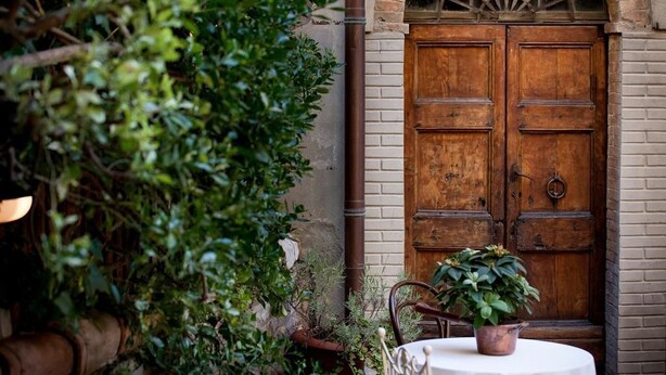 An outdoor seating area with a table and chairs, a wooden door, and potted plants. - Il Palazzo Boutique B&B (Montalcino)