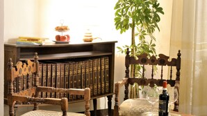 A wooden chair with a woven seat, a bookshelf with books, a small table with a bottle and glasses, and a potted plant. - Il Palazzo Boutique B&B (Montalcino)