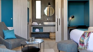 Une chambre d’hôtel moderne comprenant un canapé, une petite table, un lit, une salle de bain avec un miroir et une table de chevet.
