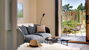 Un salon moderne avec un canapé gris, une petite table ronde et un fauteuil rouge. Un chapeau de paille et un tapis blanc à poils longs sont posés sur le sol.