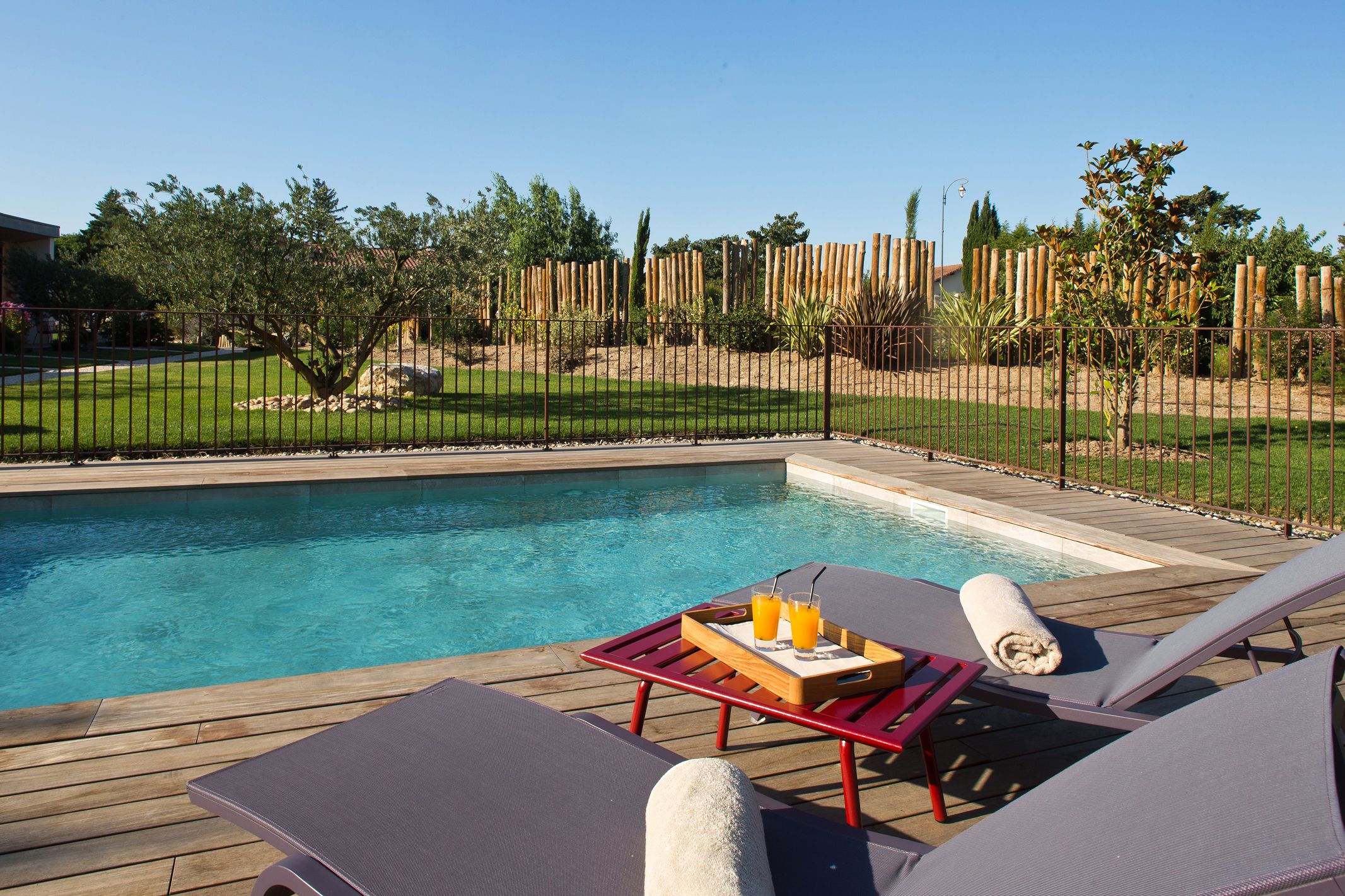 A poolside area with lounge chairs, a wooden deck, and a table with a tray of drinks.