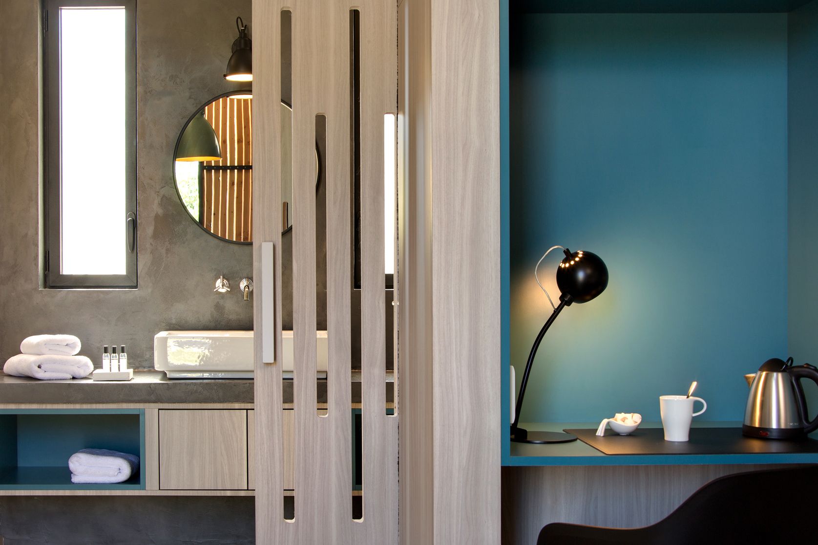 A modern room with a wooden partition, a mirror, a desk with a lamp, a kettle, and a cup.