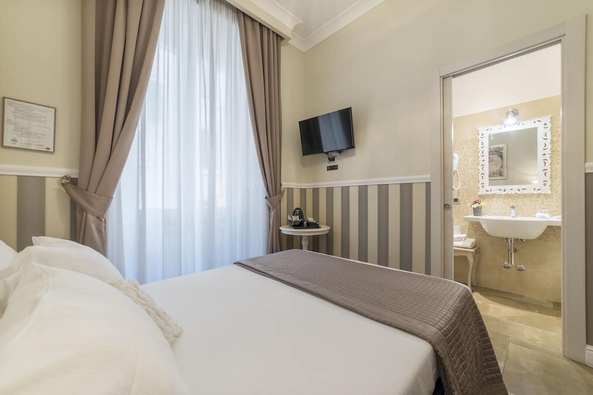 Une chambre d’hôtel avec un lit, une télévision, une table de chevet et une salle de bain visible à travers une porte ouverte.