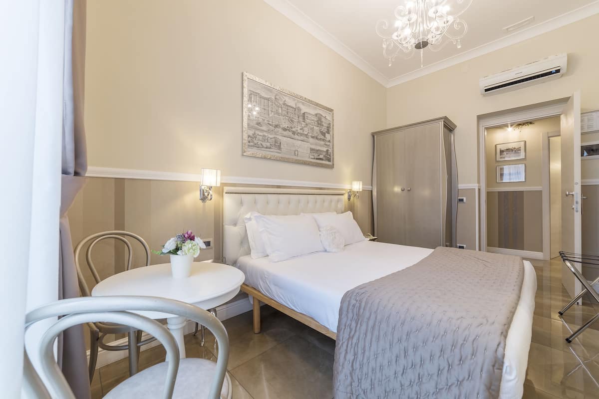 Une chambre d’hôtel avec un lit, une table de chevet, une chaise et un lustre.