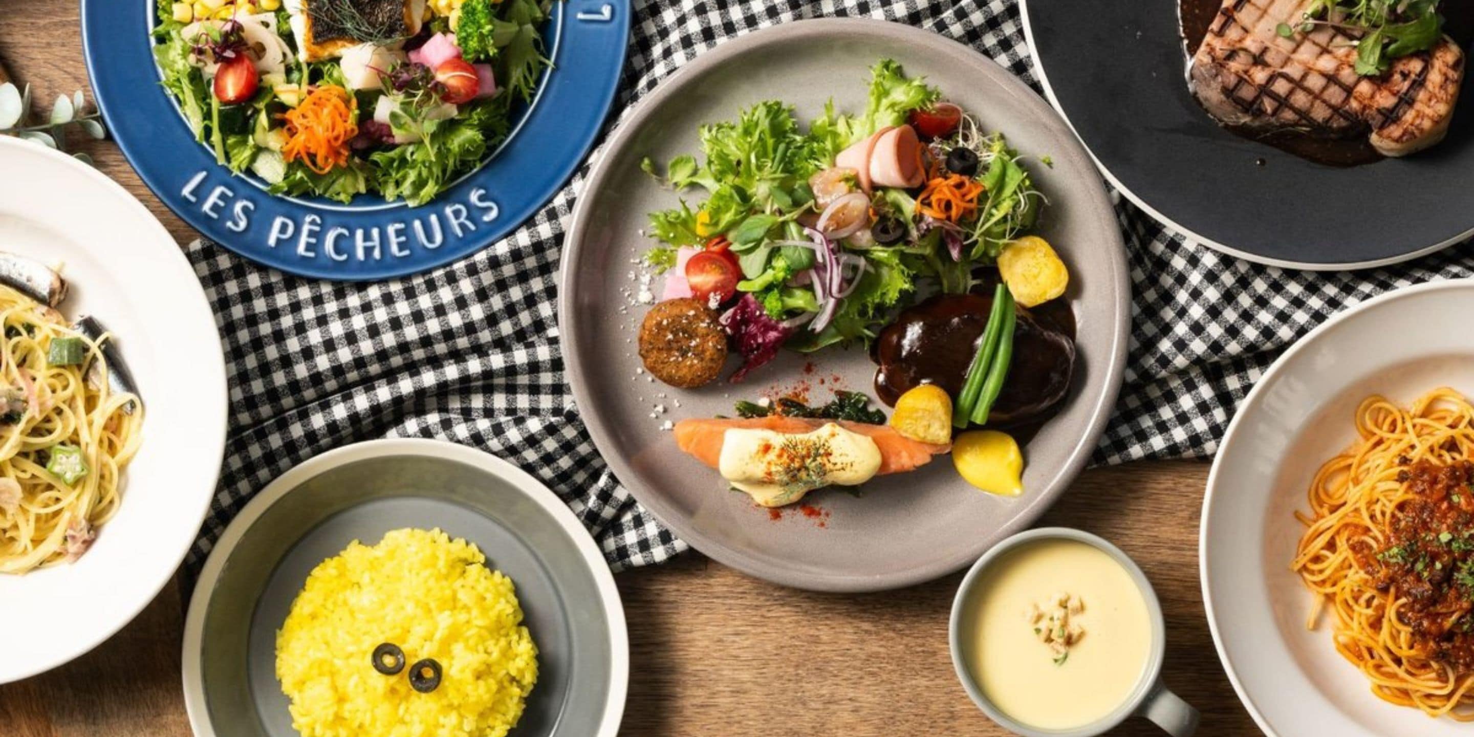 Une variété de plats, notamment une salade, des pâtes et de la viande grillée, disposés sur une nappe à carreaux.
