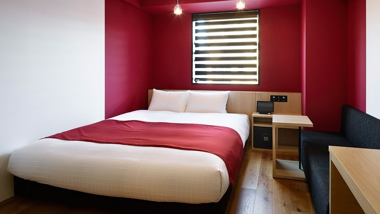 Une chambre à coucher avec un lit, un bureau, une chaise et une fenêtre avec des stores.